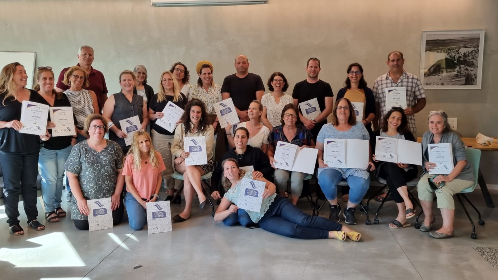 משתתפי ומשתתפות קורס הגישור הראשון לממלאי וממלאות תפקידים בקיבוצים, בתמונה קבוצתית עם תעודות הסיום