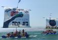 נערי ונערות בית קמה שטים בכנרת עם המפרשים שציירו לזכרן של טל היימן וענת טל קטלב